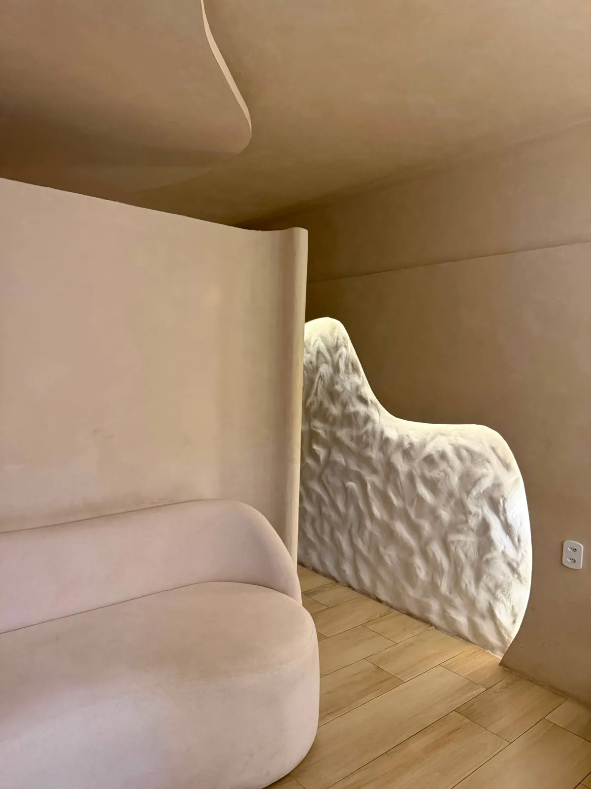 Sala do Espaço Matú com sofá curvo, parede texturizada e iluminação suave