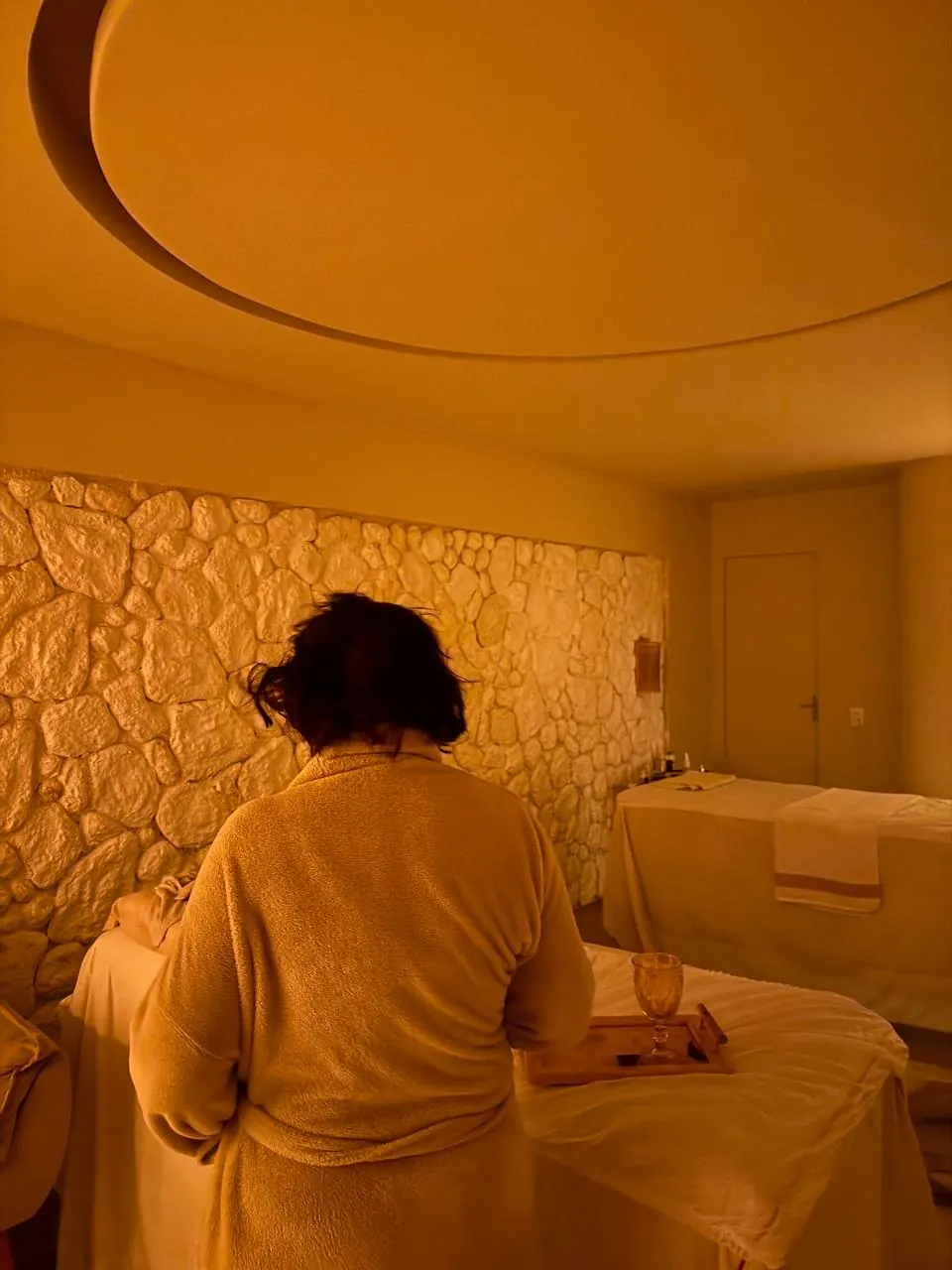 Pessoa de roupão em sala com luz âmbar e parede de pedra